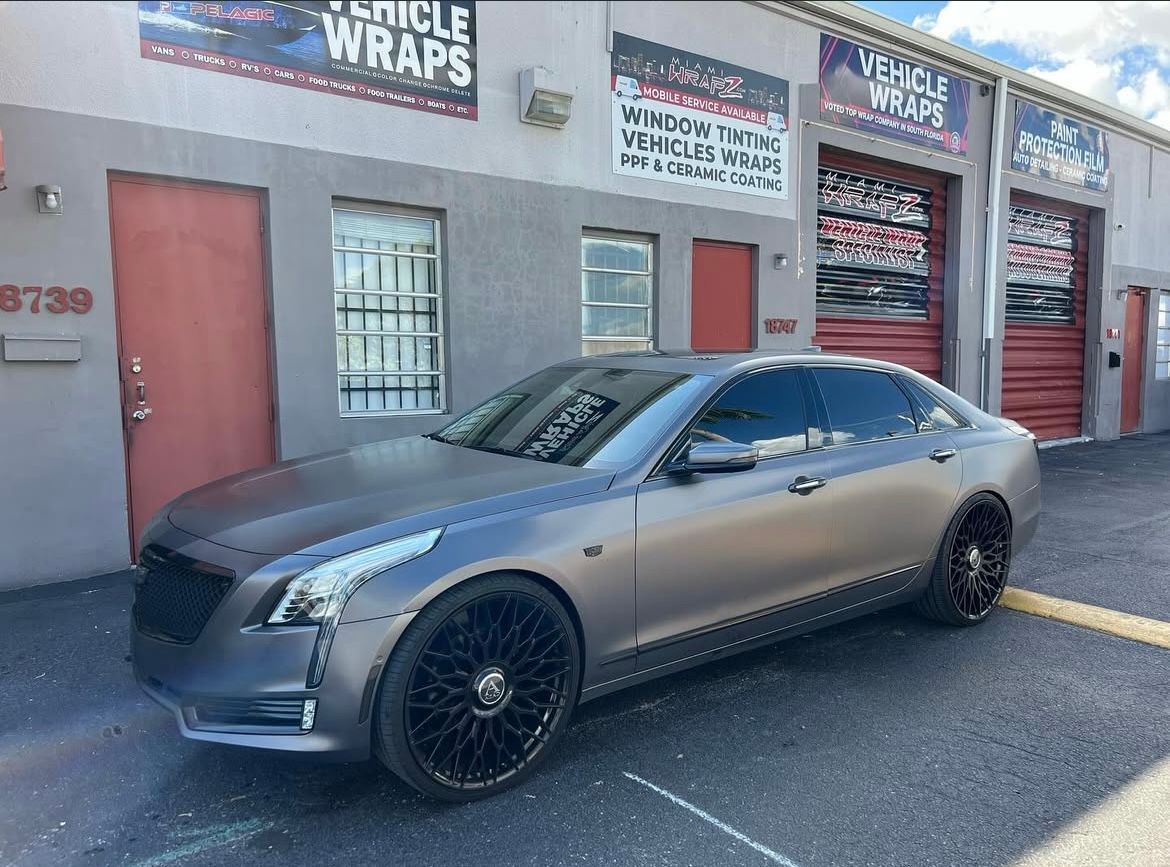 A car is parked in front of a building that says vehicle wraps.