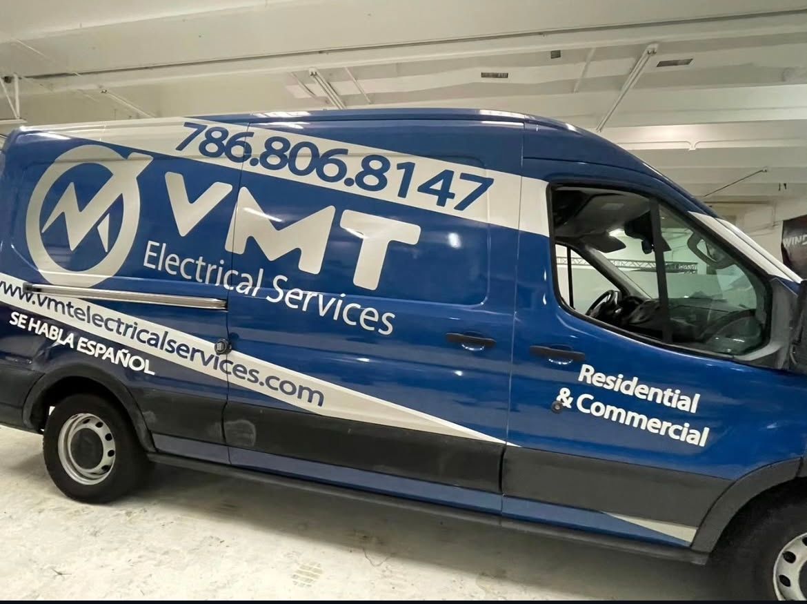A blue van with electrical services written on the side is parked in a garage.