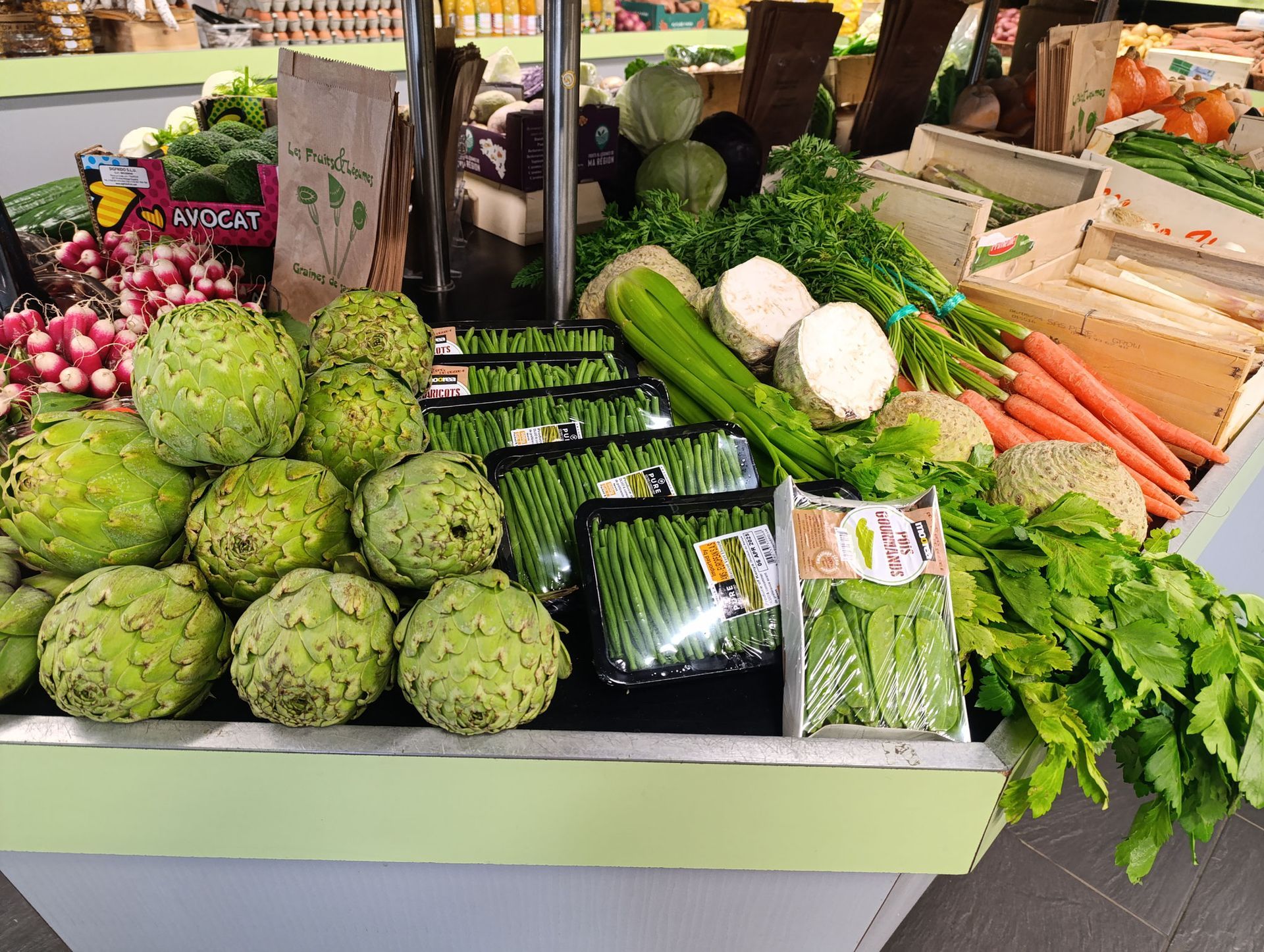 Un étalage de légumes frais sur un marché, notamment des artichauts, des asperges, des carottes et des radis.