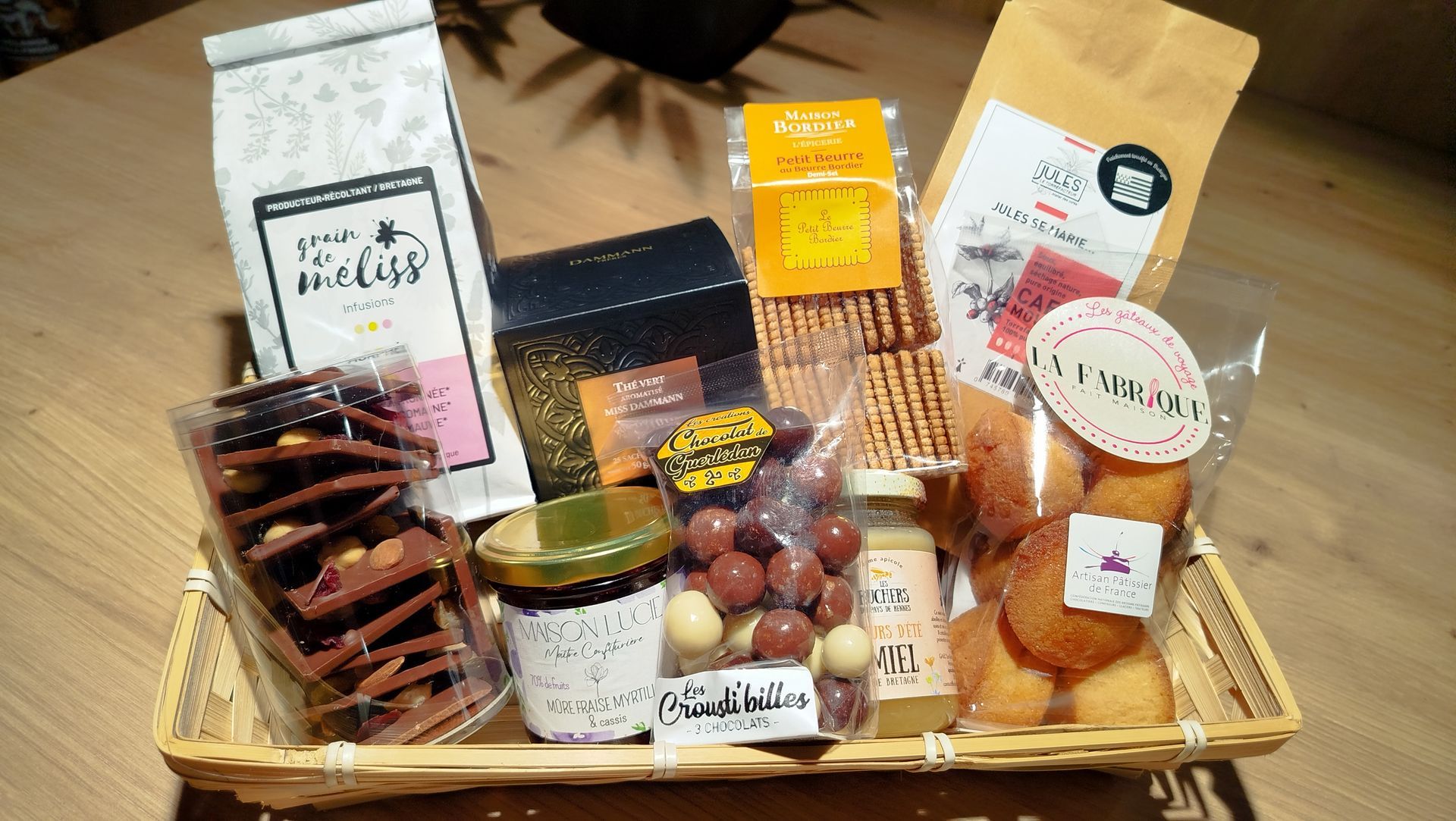 Panier-cadeau rempli de produits, notamment des olives, du pâté, de la charcuterie, des craquelins et des bouteilles de vin.