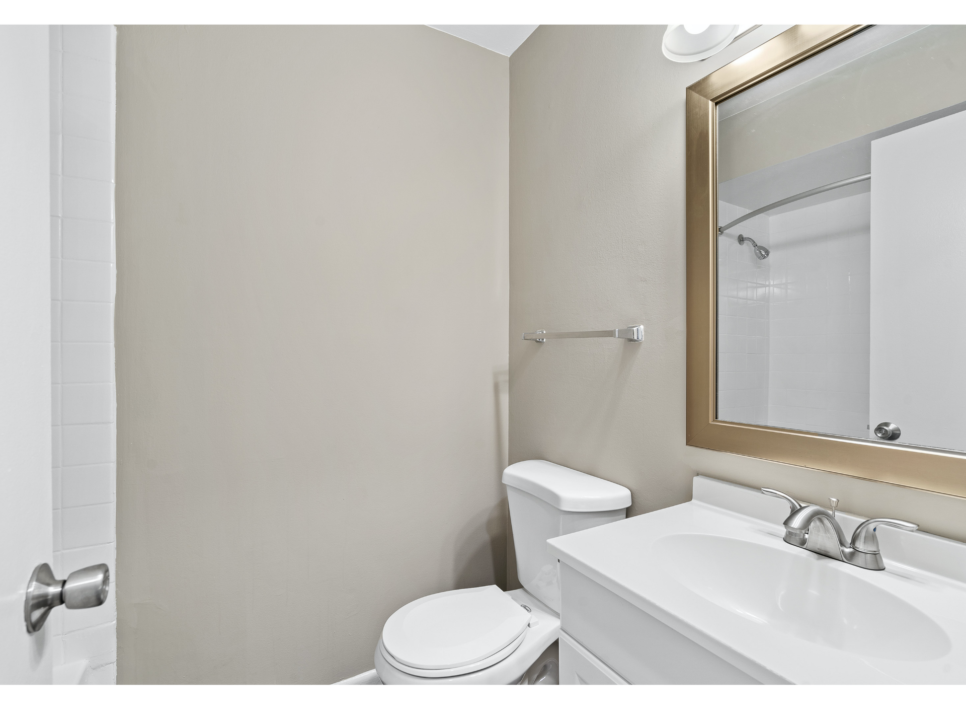 Bathroom in an apartment: beige walls, toilet, sink, and a large framed mirror.