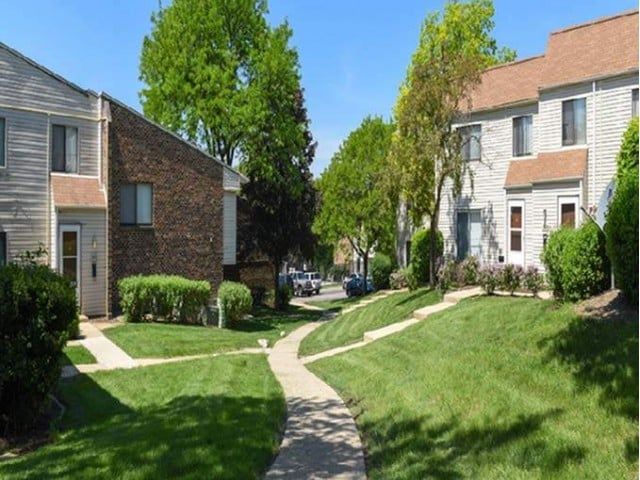 Exterior view of a garden-style apartment community with walkways, lawns, and trees.