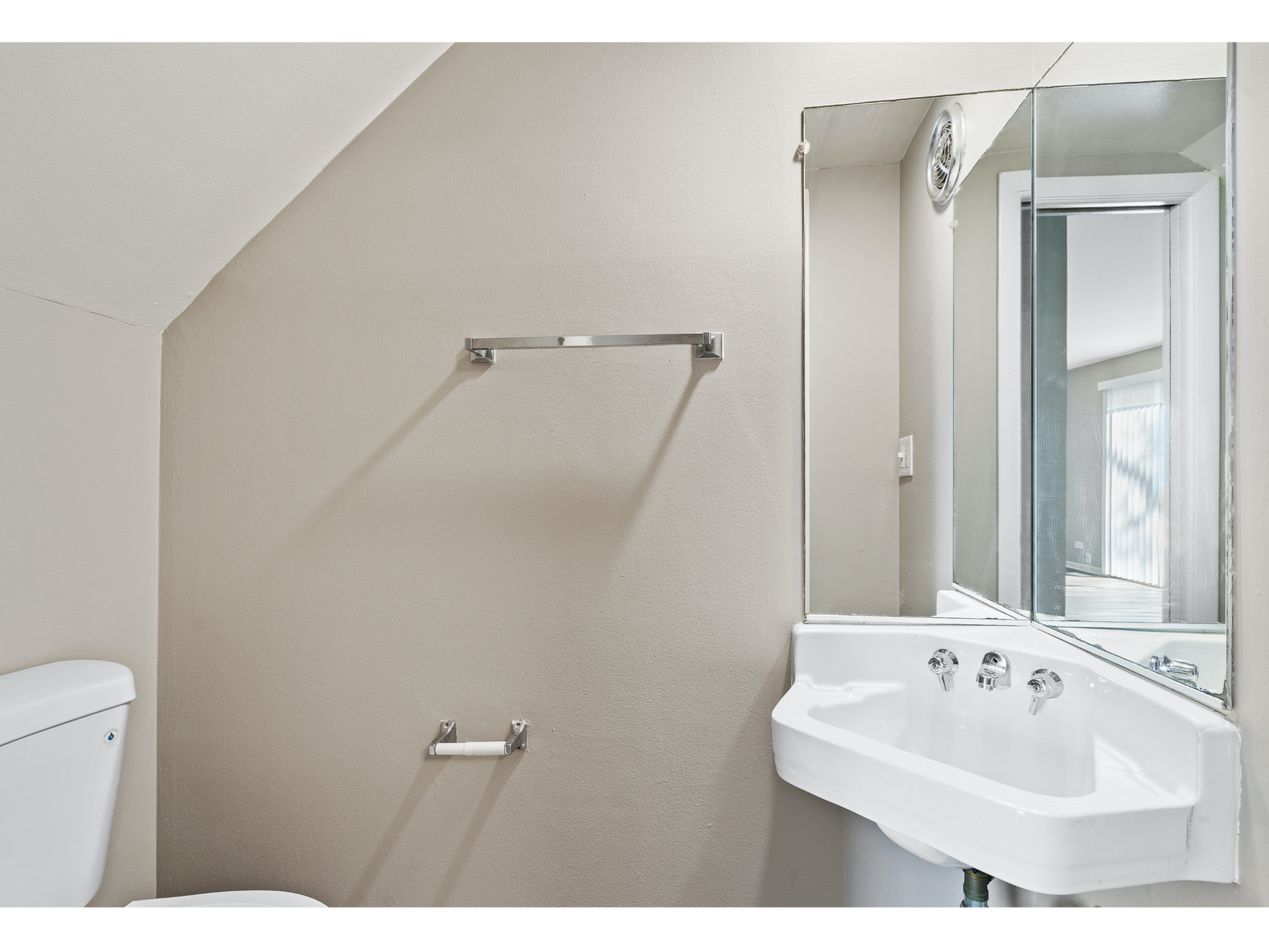 Small bathroom with a white sink, large mirror, toilet, and towel bar on beige walls.