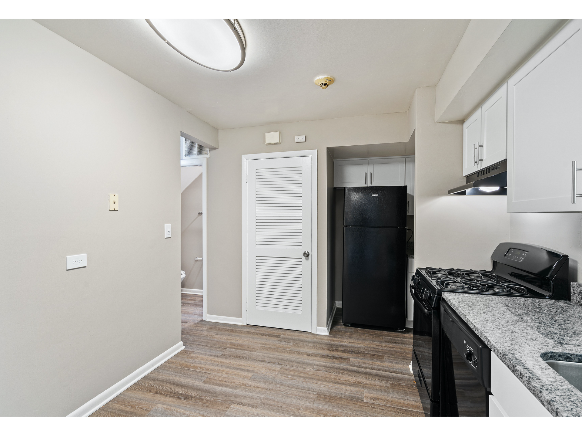Kitchen area with black refrigerator, stove, white cabinets, and granite countertops.