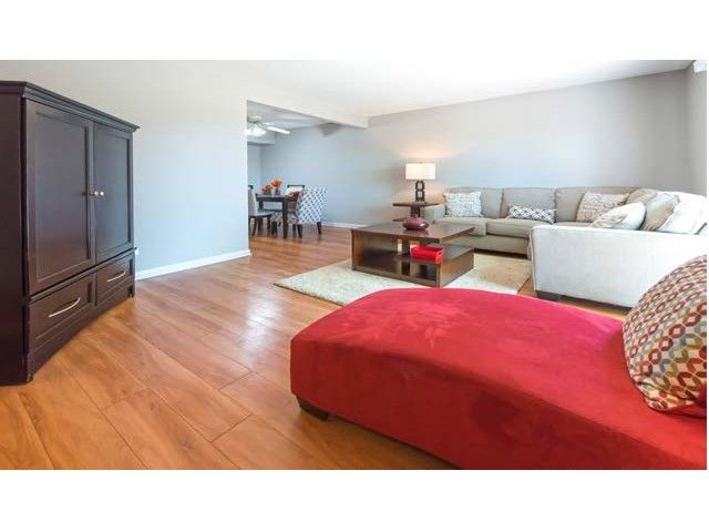 Living room with wood floors, beige sofa, red ottoman, coffee table, and dark armoire.