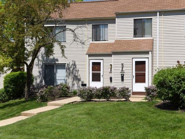 Exterior of a townhouse-style multifamily building with two brown doors, steps, and landscaped lawn.