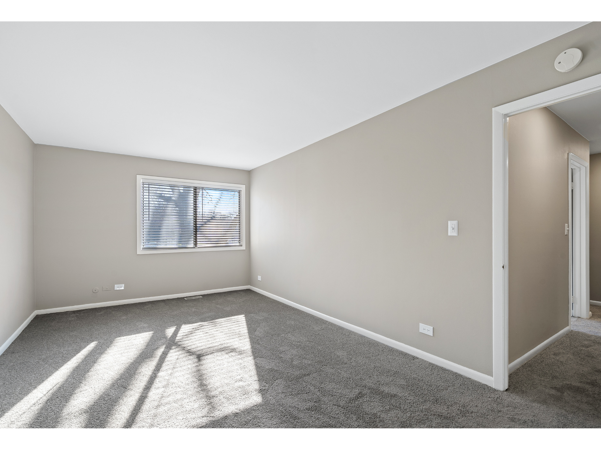 Empty beige carpeted bedroom with window and doorway