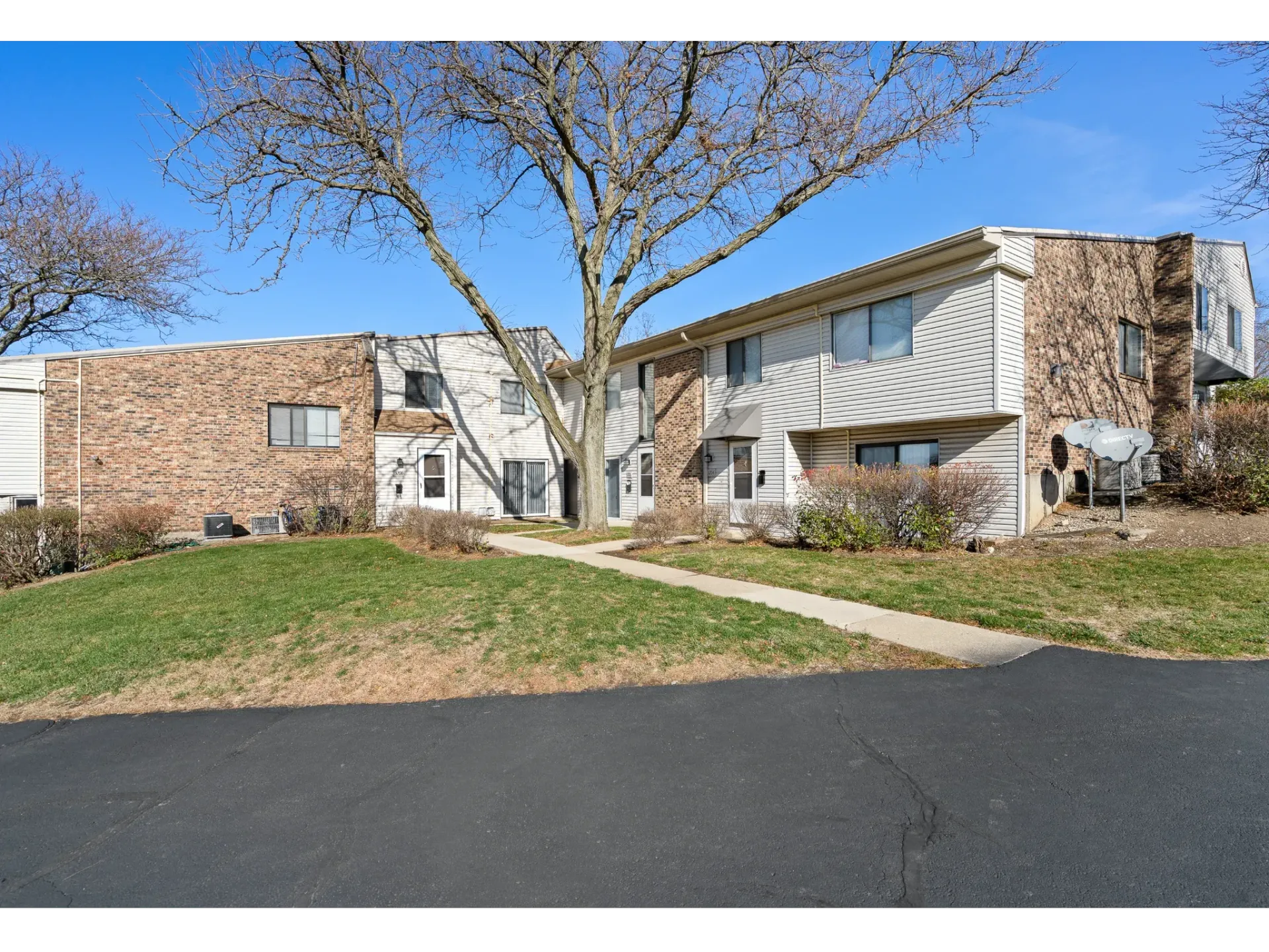 Exterior view of a multi-unit apartment building with brick and beige siding, trees, and a walkway.