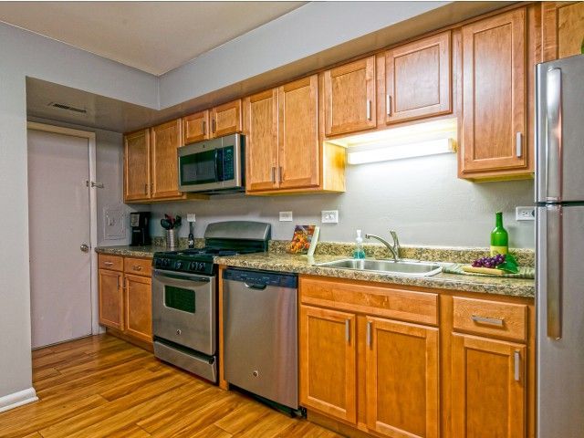 Apartment kitchen with wooden cabinets, granite counters, stainless steel stove, dishwasher, and sink.