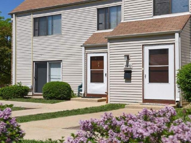 Exterior view of a beige apartment building with two front doors and landscaped shrubs.