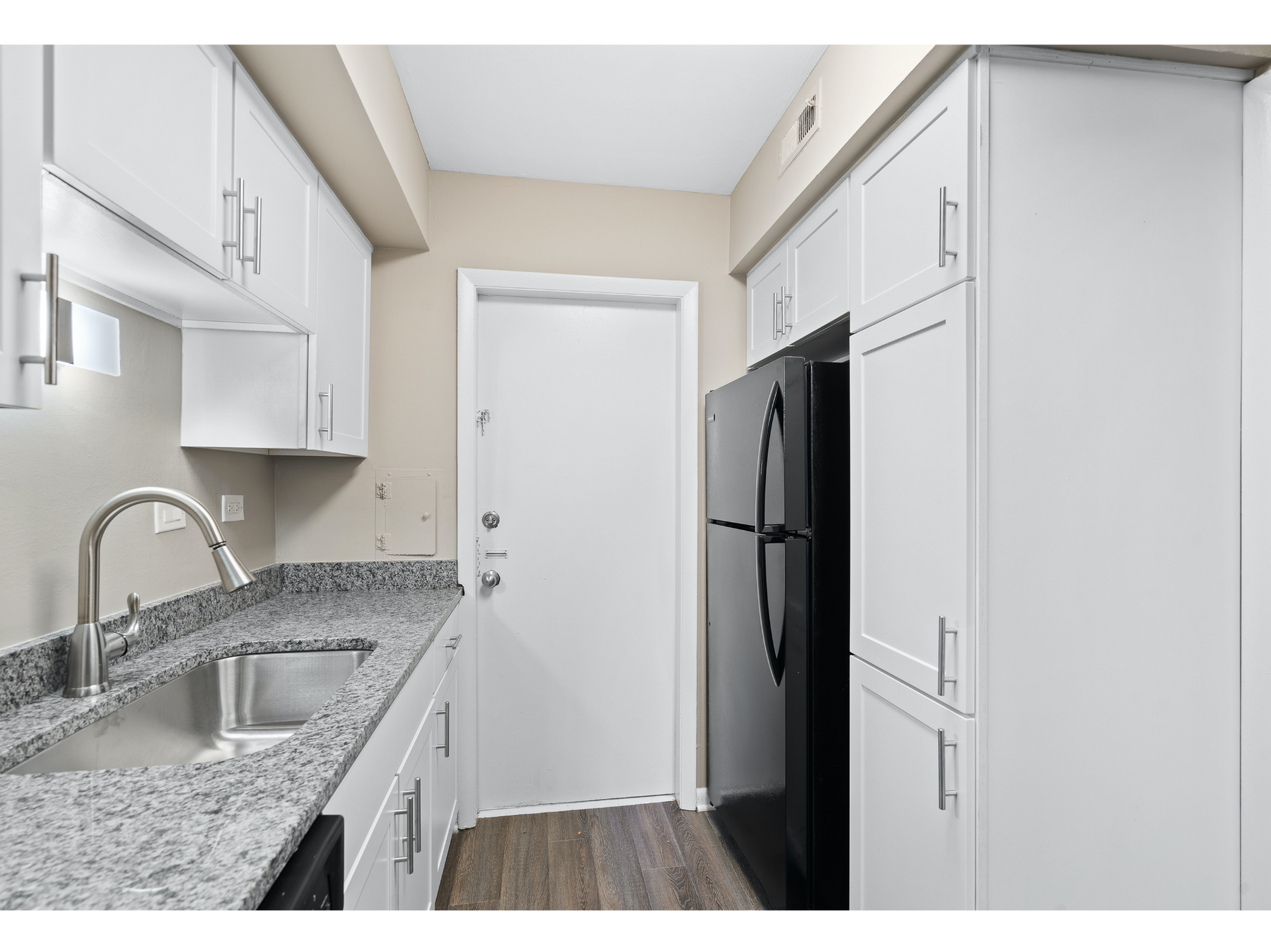 White kitchen with granite countertops, stainless steel sink, and a large refrigerator.