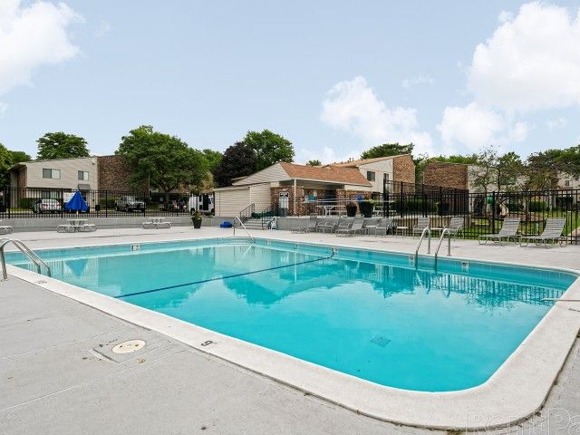 Outdoor community pool at an apartment complex with lounge chairs and fencing.