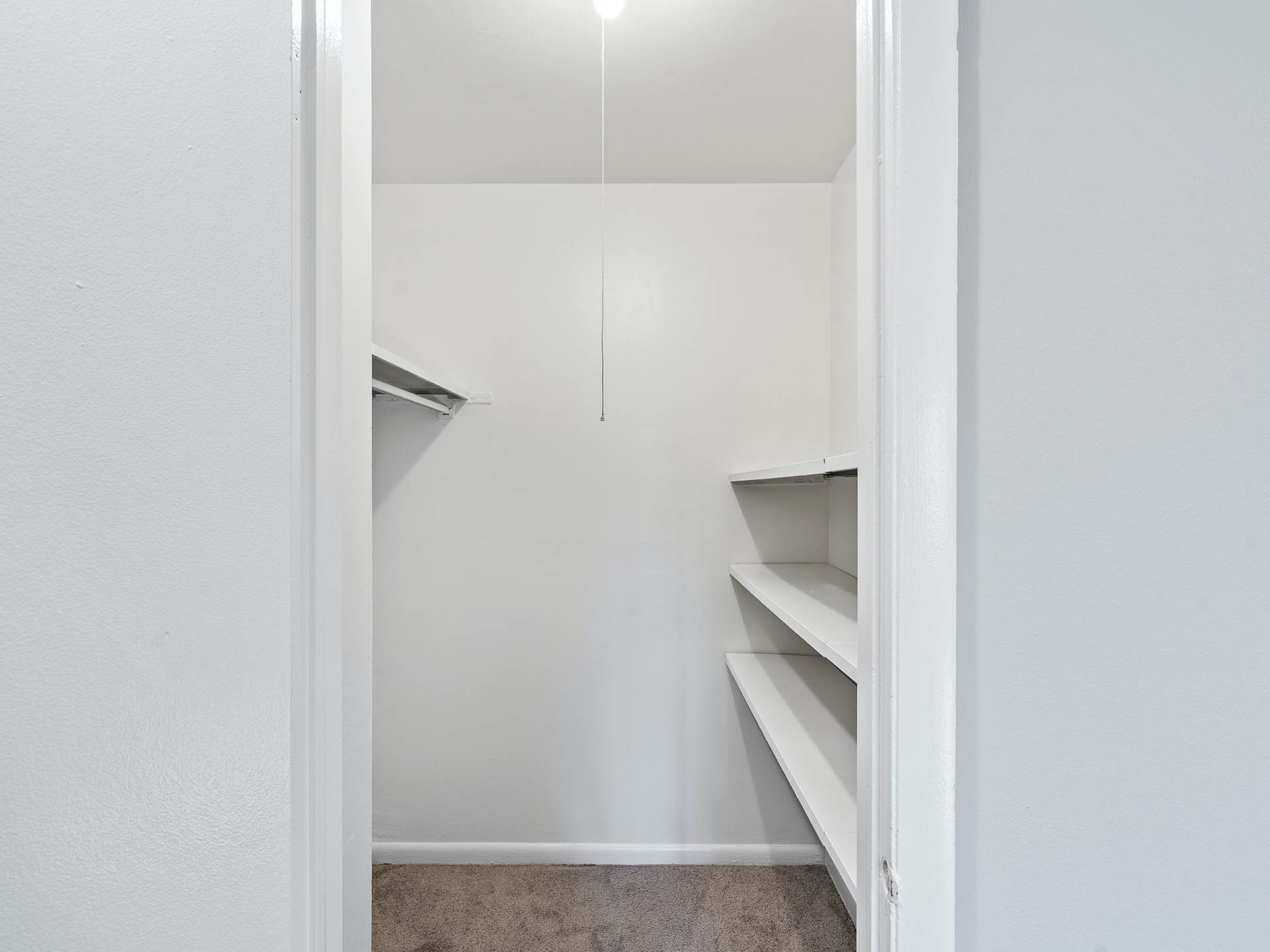 Walk-in closet with white shelves along the right wall and a hanging rod.