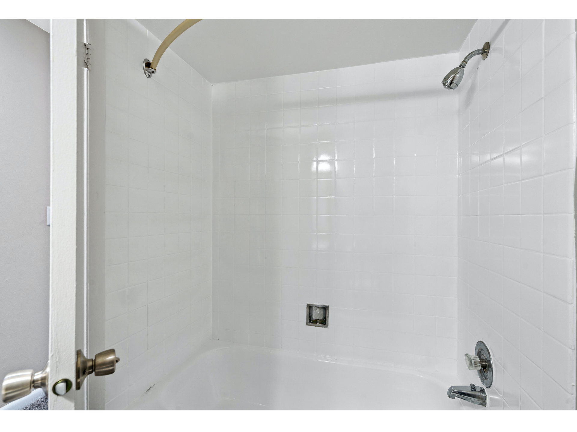 White-tiled shower and bathtub with chrome fixtures in a compact bathroom.