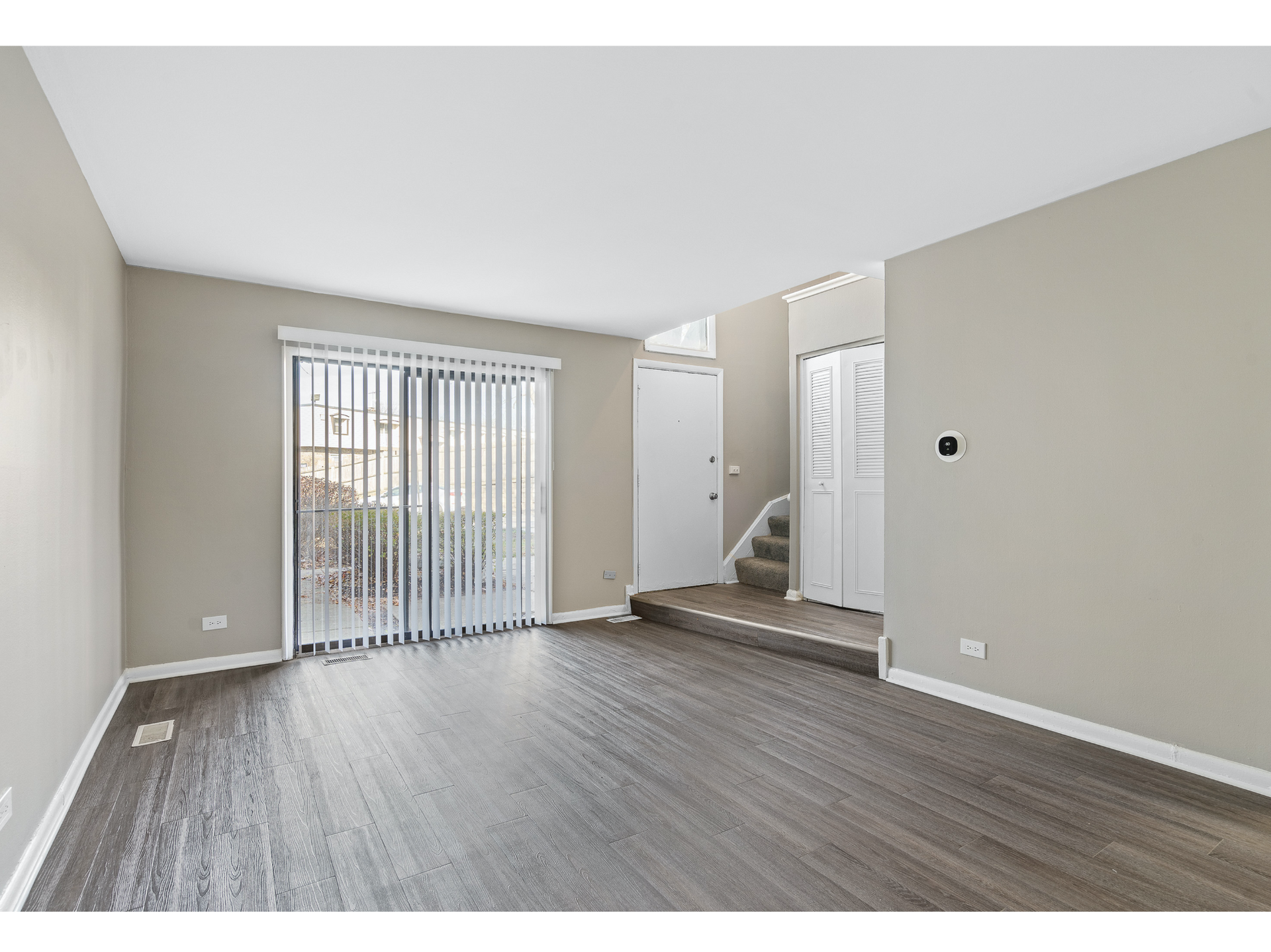 Living room with sliding glass door to patio, vertical blinds, and entry stairs visible.