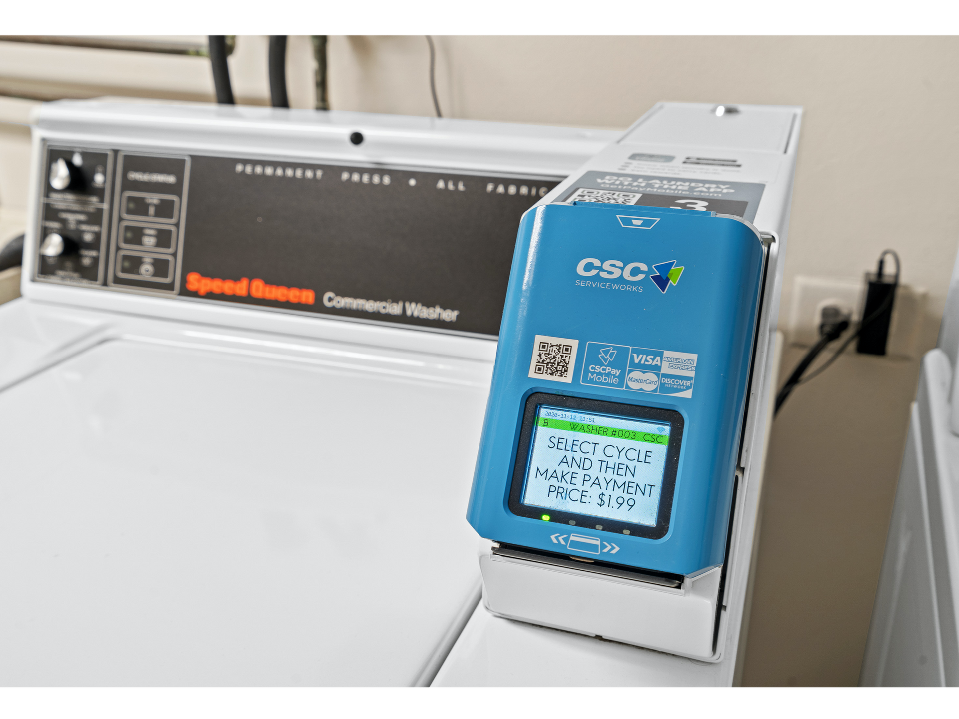 Blue payment terminal on a Speed Queen commercial washer in a communal laundry room.