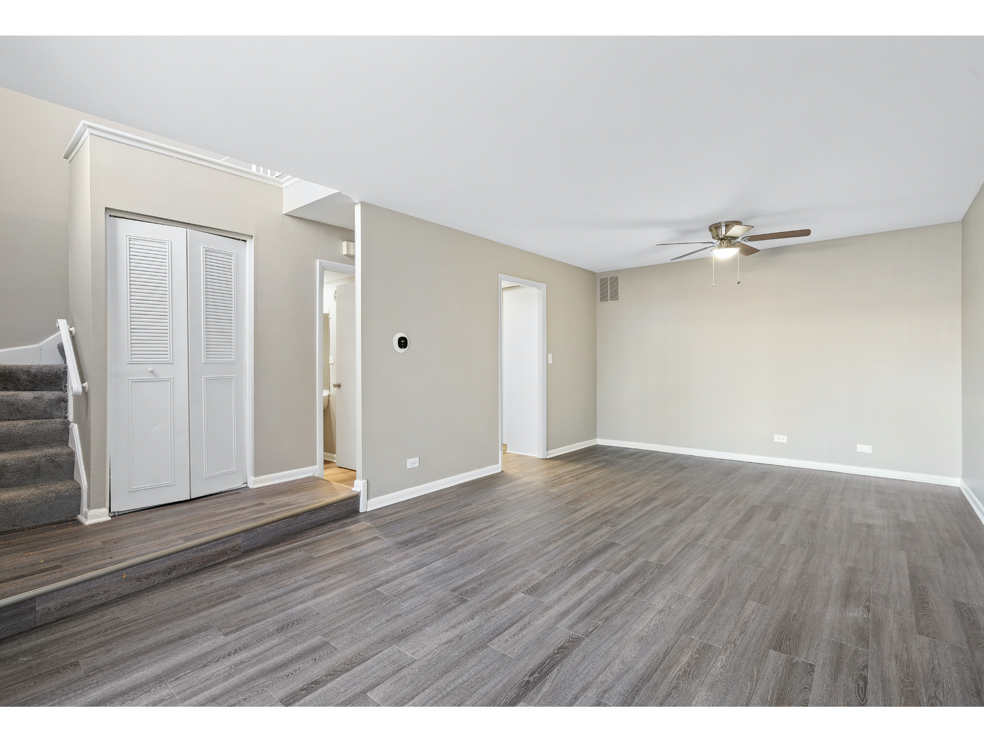 Interior of a finished basement living area with stairs, gray walls, and a ceiling fan.