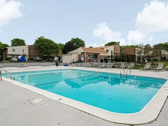 Swimming pool with lounge chairs, surrounded by trees and apartment buildings at Townhomes at Highcrest in Woodridge, IL.
