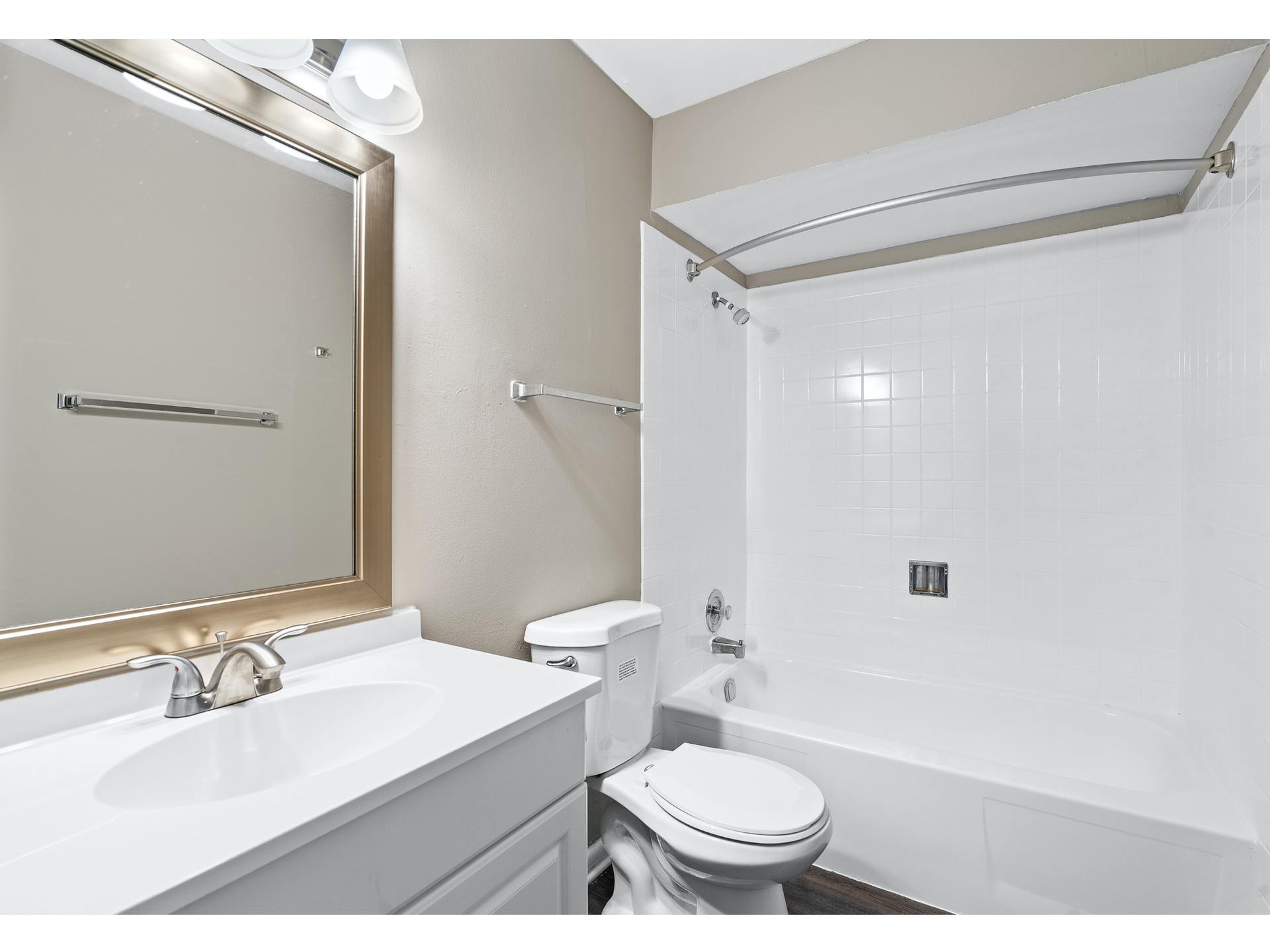 Bathroom with vanity sink, large framed mirror, toilet, and white tile bathtub/shower with curved rod.