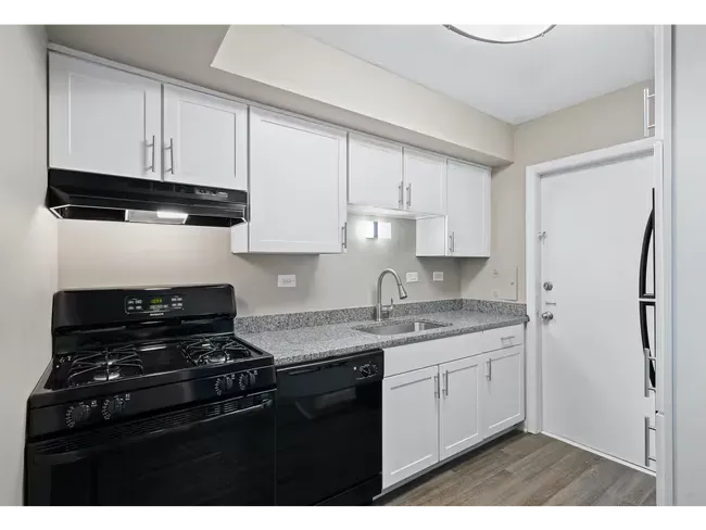 Small white kitchen with black appliances, gray countertops, and light wood floors at Townhomes at Highcrest in Woodridge, IL.