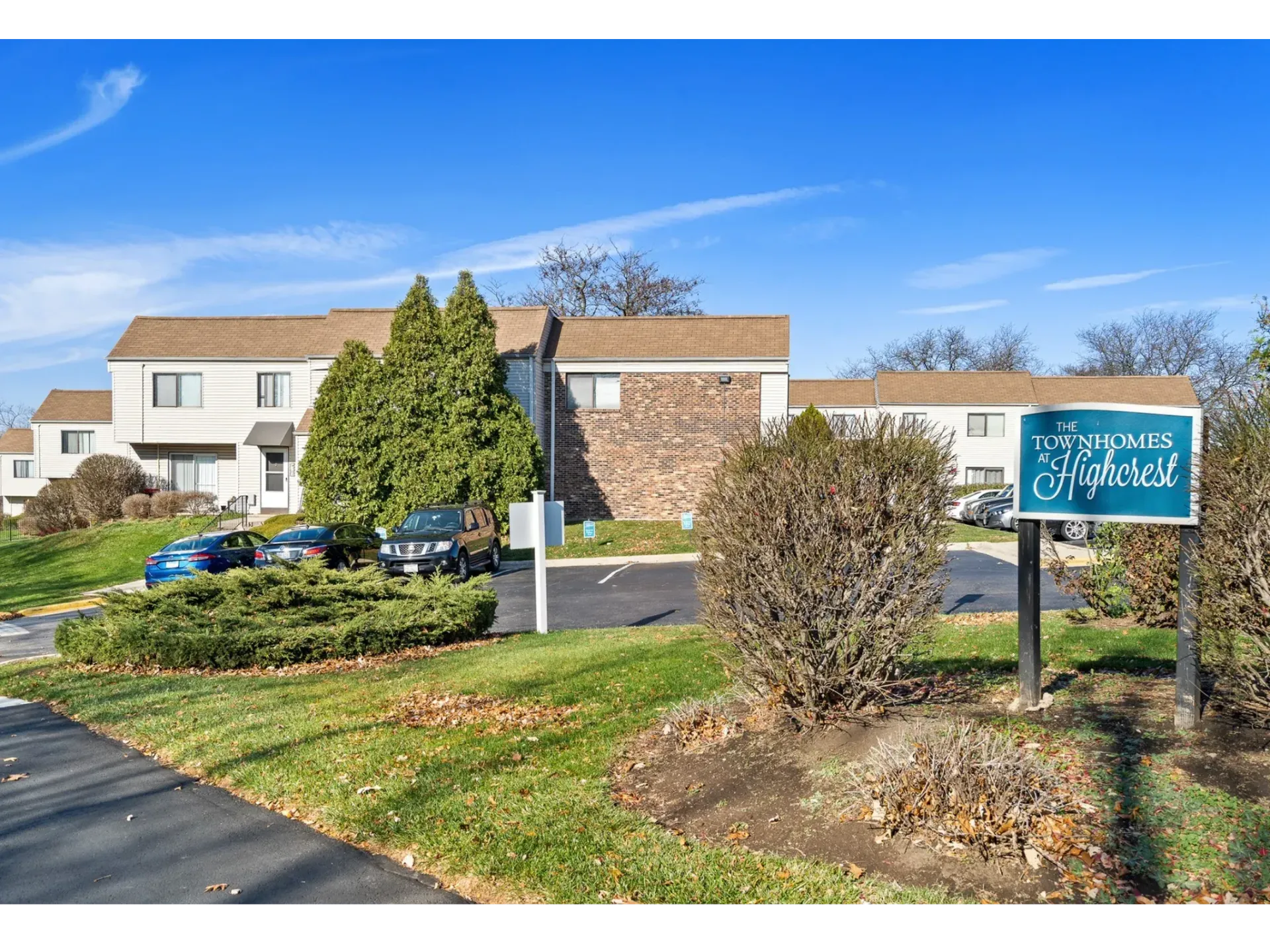 Exterior view of The Townhomes at Highcrest community with sign, cars, and landscaping.
