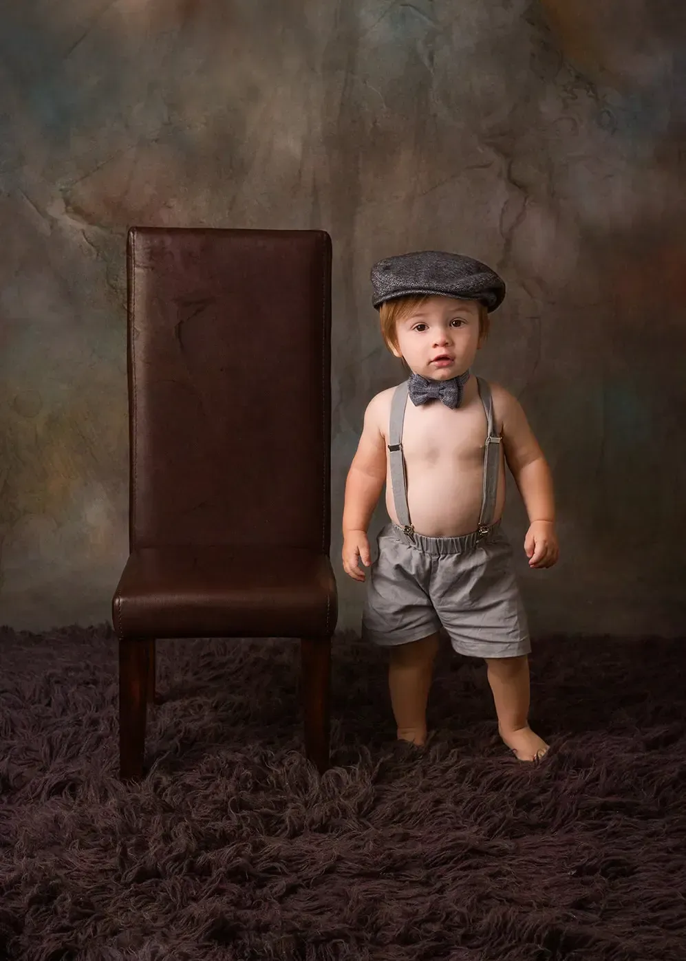 9 Month old phto shoot., Boy in newsboy cap standing next to a chair.