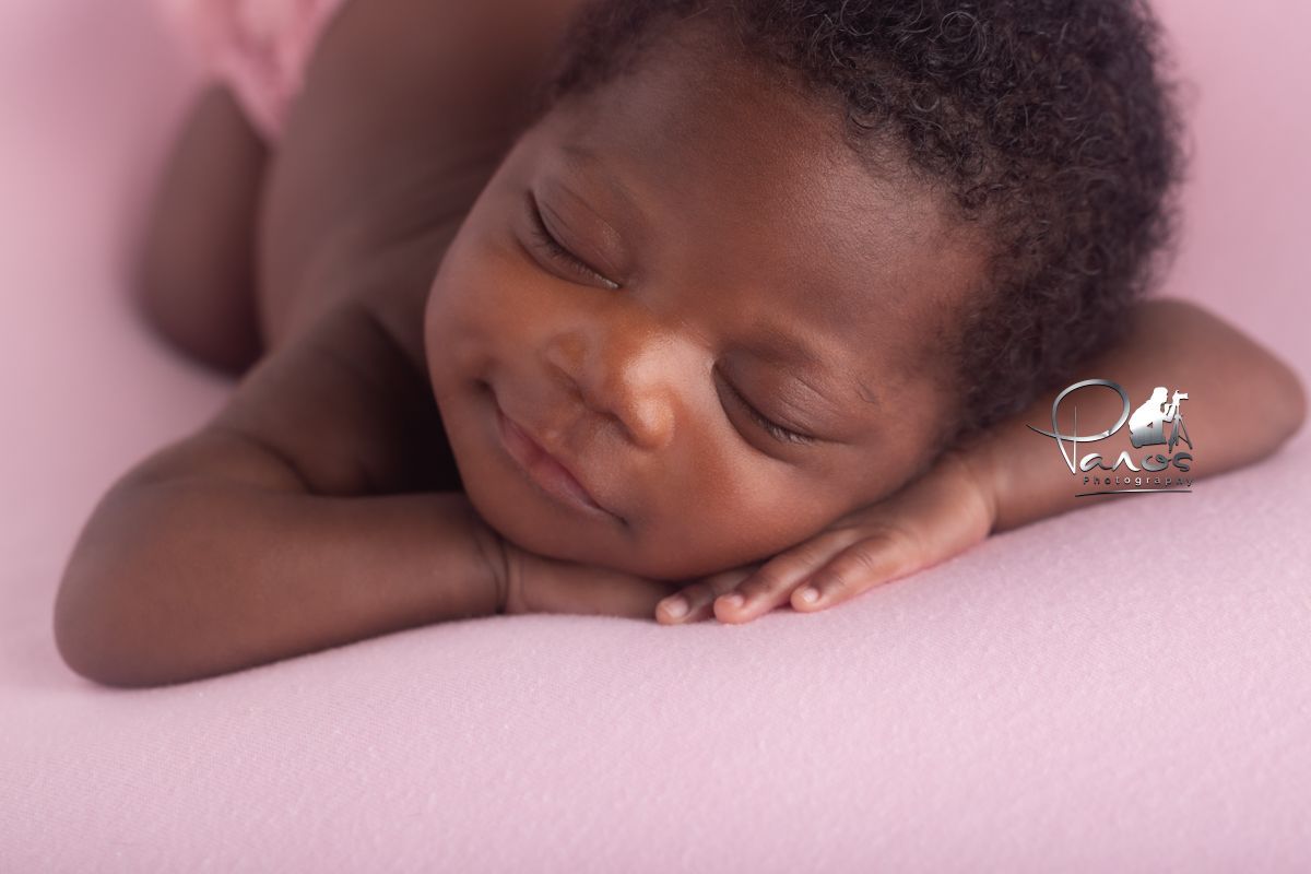 African American newborn girl with cheek on hands, sleeping.