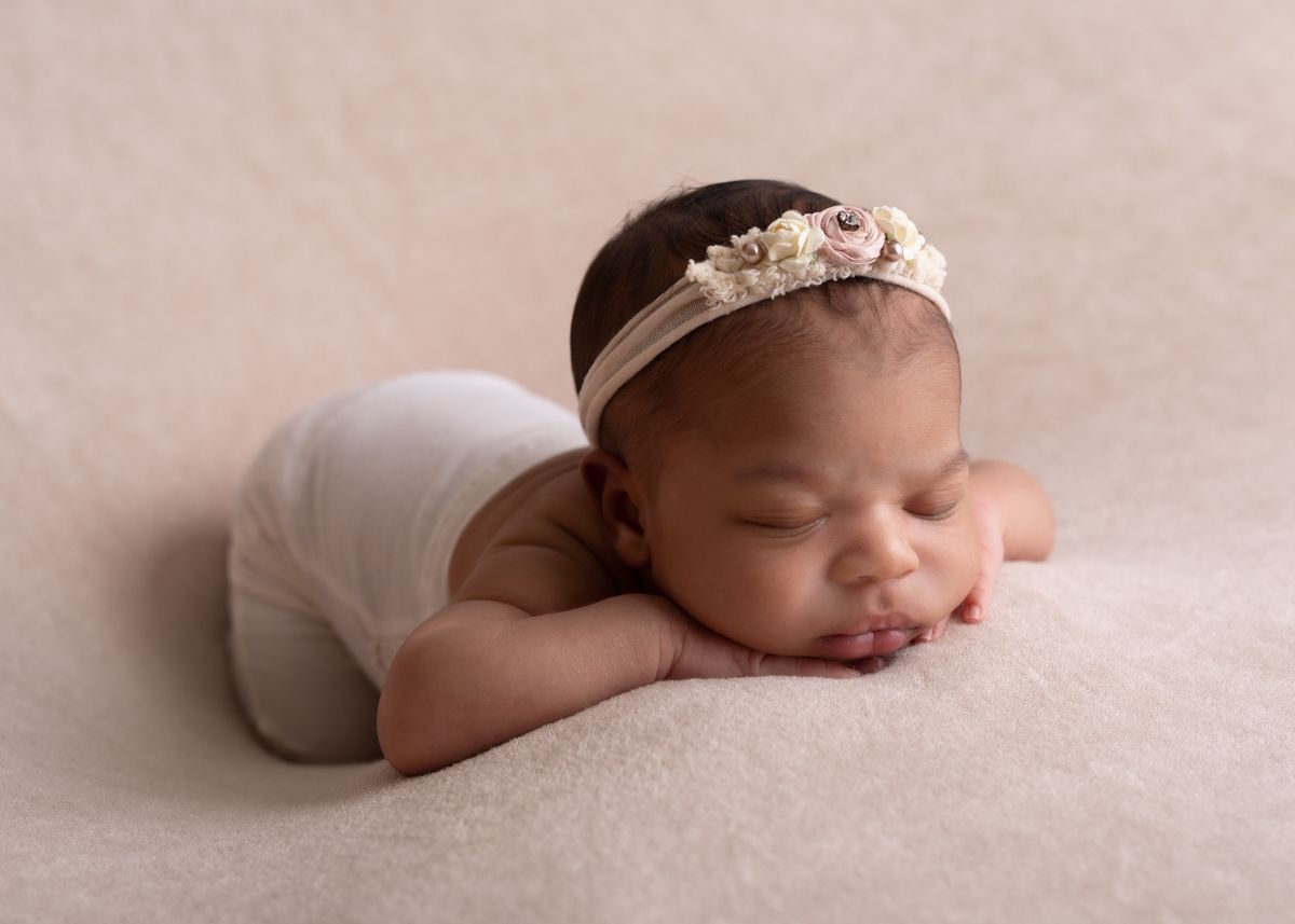 African American newborn girl with chin on hands, sleeping.