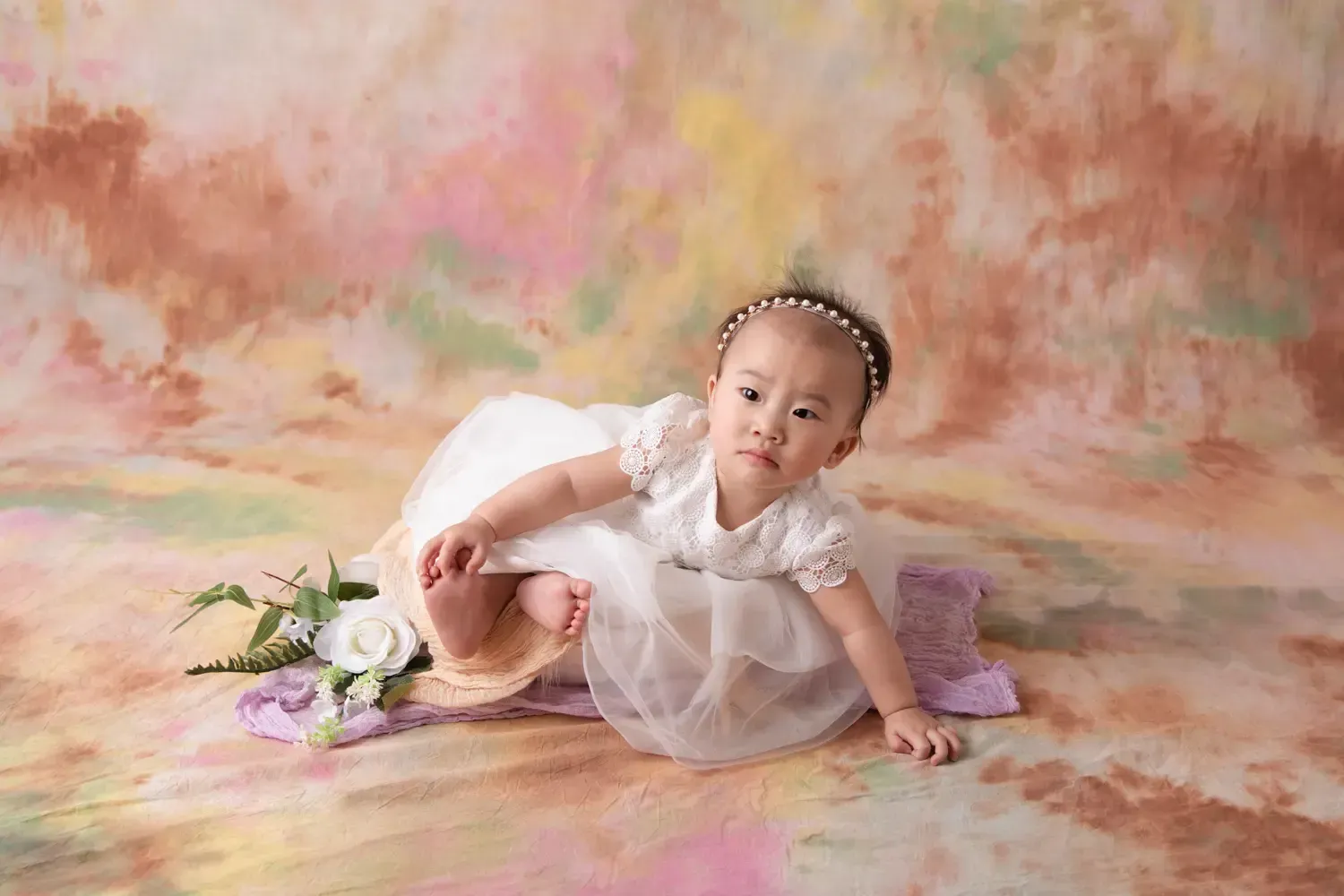 9 month old girl in white dress on background with lots of pastel colors. 