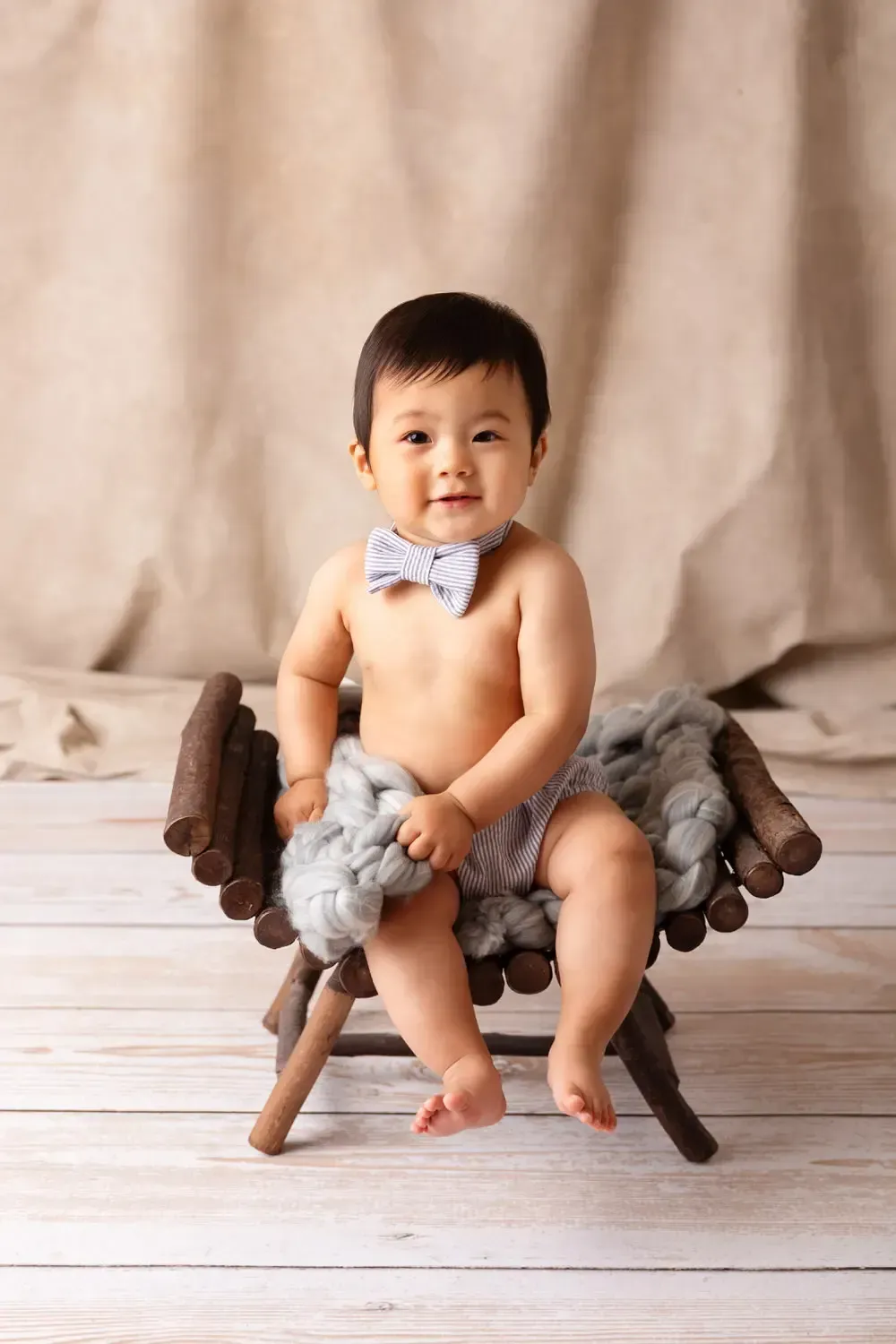 9 month old Asian baby boy on wooden curved bench. Blue pinstripe pants and bowtie