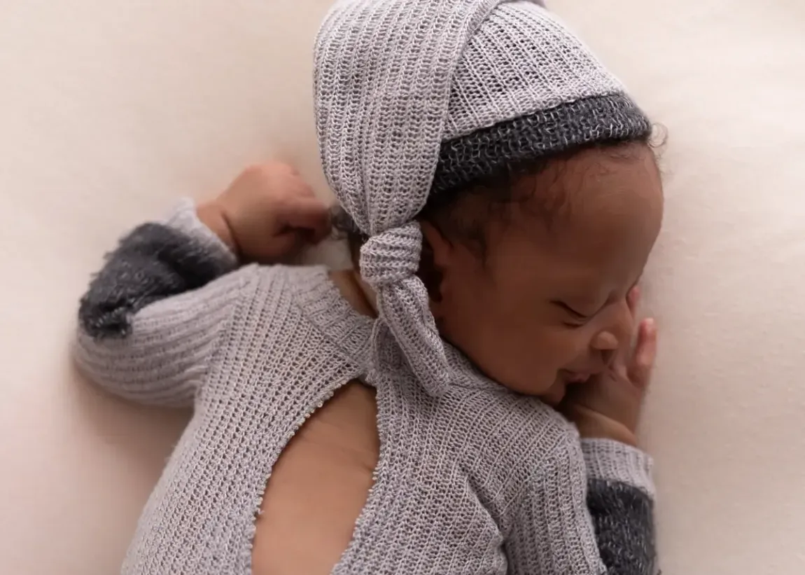 Newborn boy with cheek on hand sleeping.Wearing grey romper.