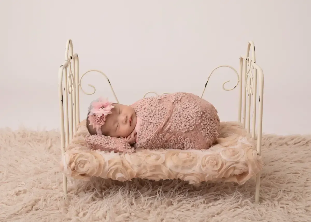 Newborn girl wrapped in pink and lying on side in wire bed.
