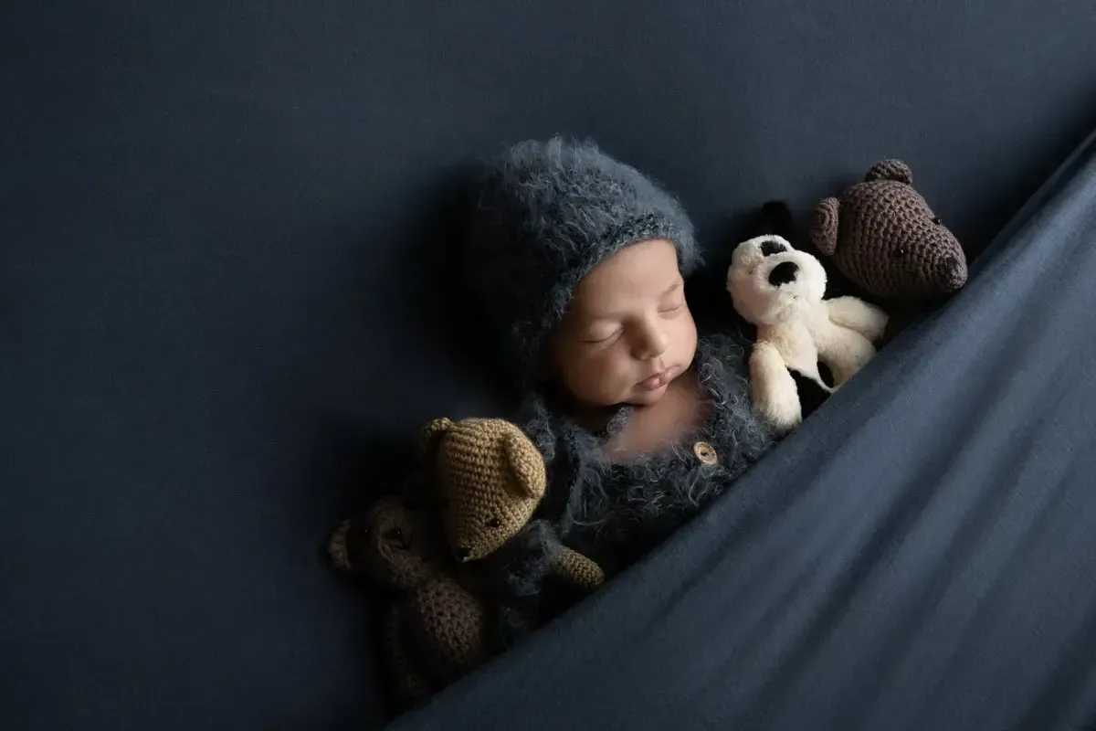 Newborn boy in Angora romper with matching bonnet tucked in sleeping.