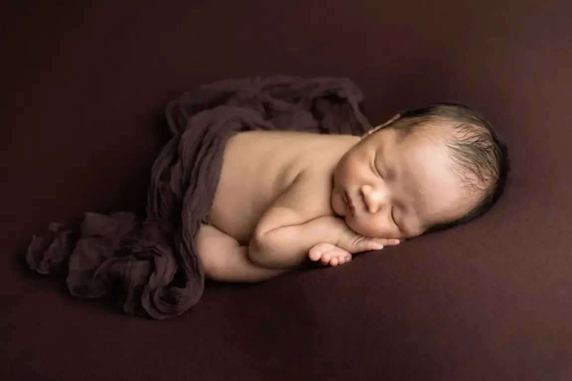 Newborn boy folded over with chin on feet. Womb pose.