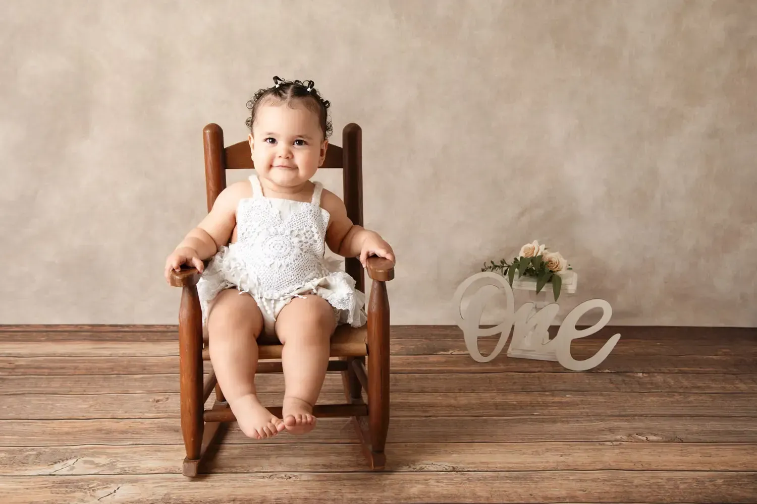 Baby girl sitting in tiny rocking chair with flowers O N E. 