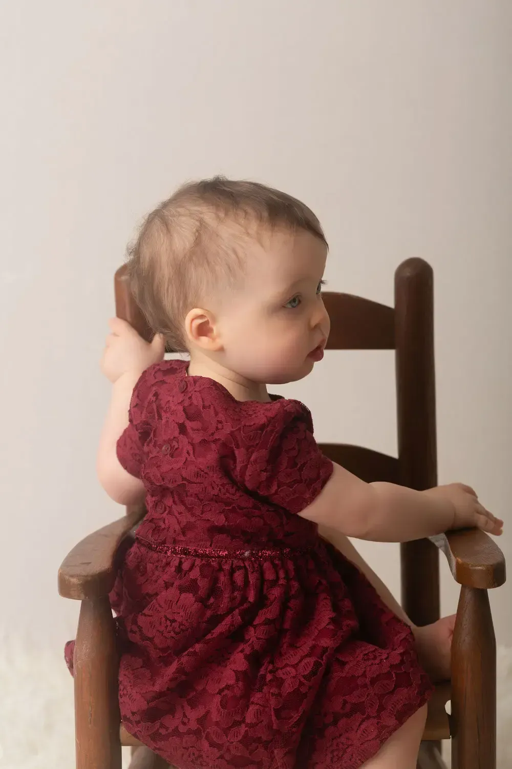 One year old birthday portrait. Girl in win colored lace dress seating in rocking chair.