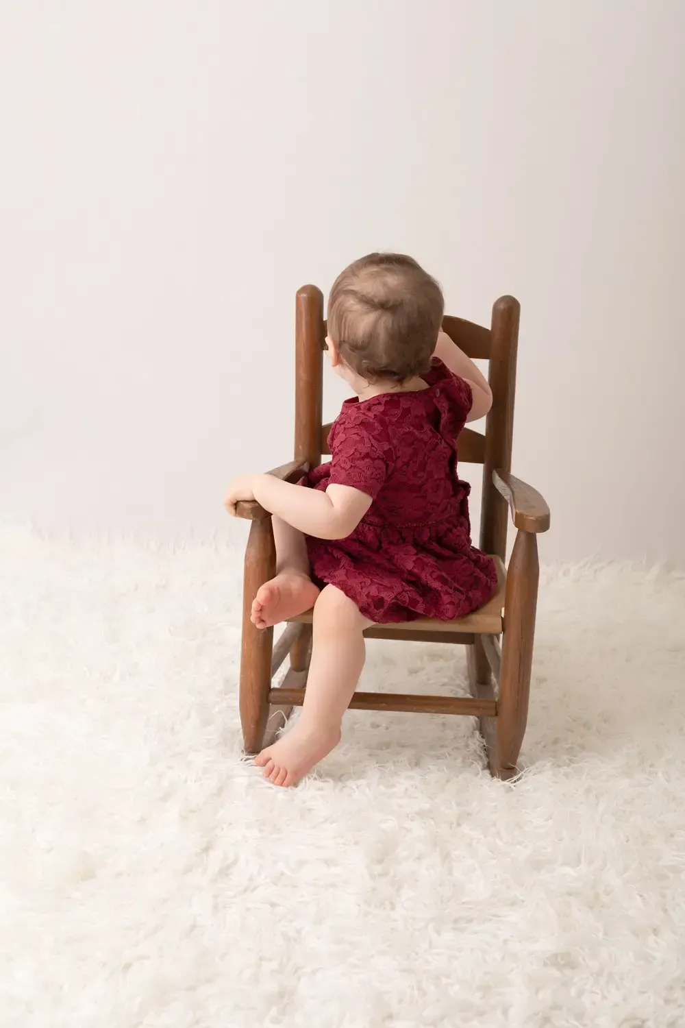 Baby girl in rocking chair. Wine colored lace dress. Cake Smash