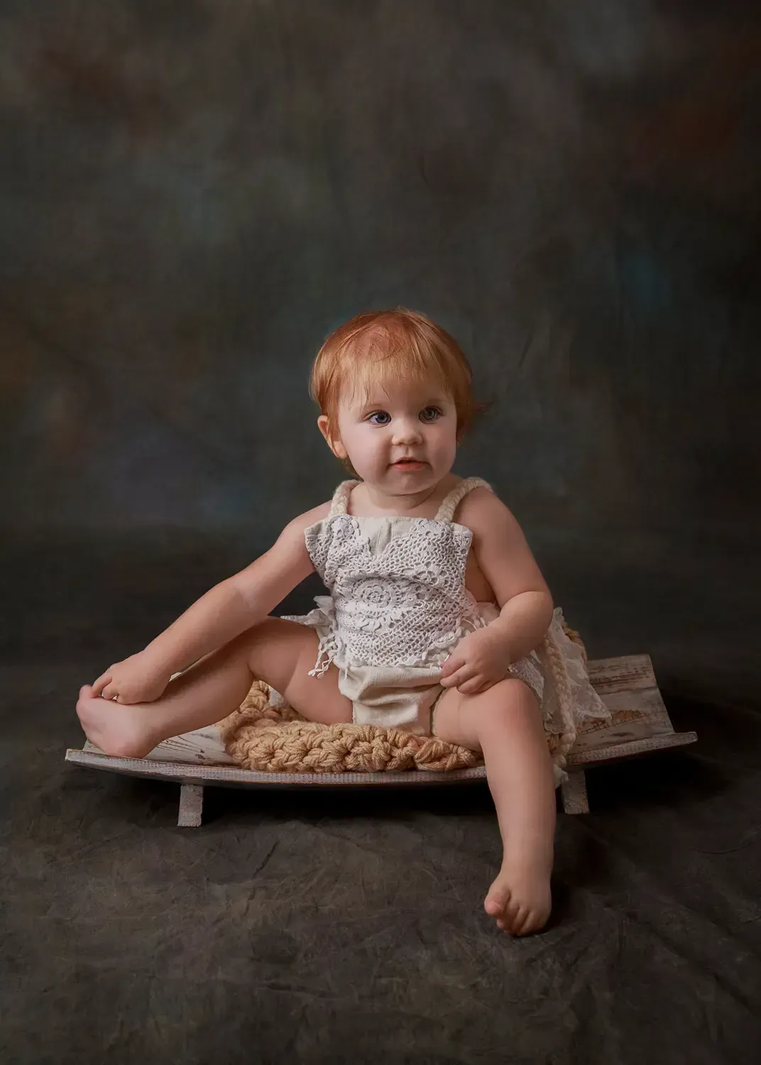 8 months girl sitting in wooden dough bowl in boho romper. Red hair. Happy.