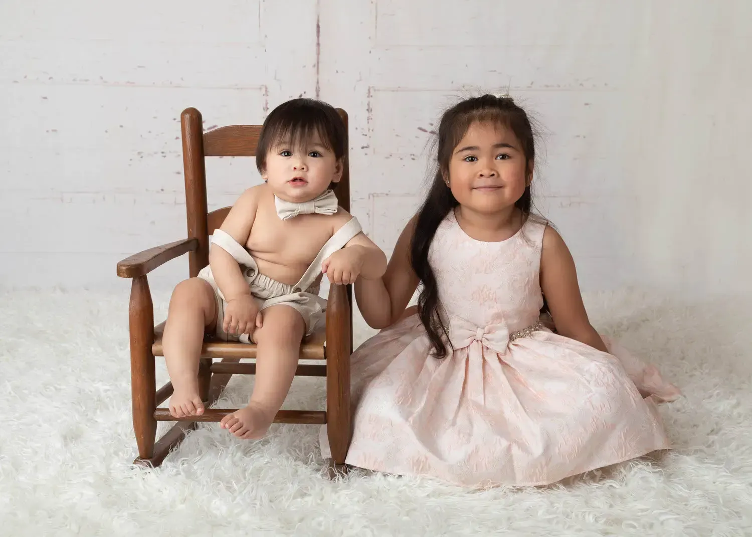 First Birthday Baby Boy. Image if boy and his older sister seatied on fluffy white rug.