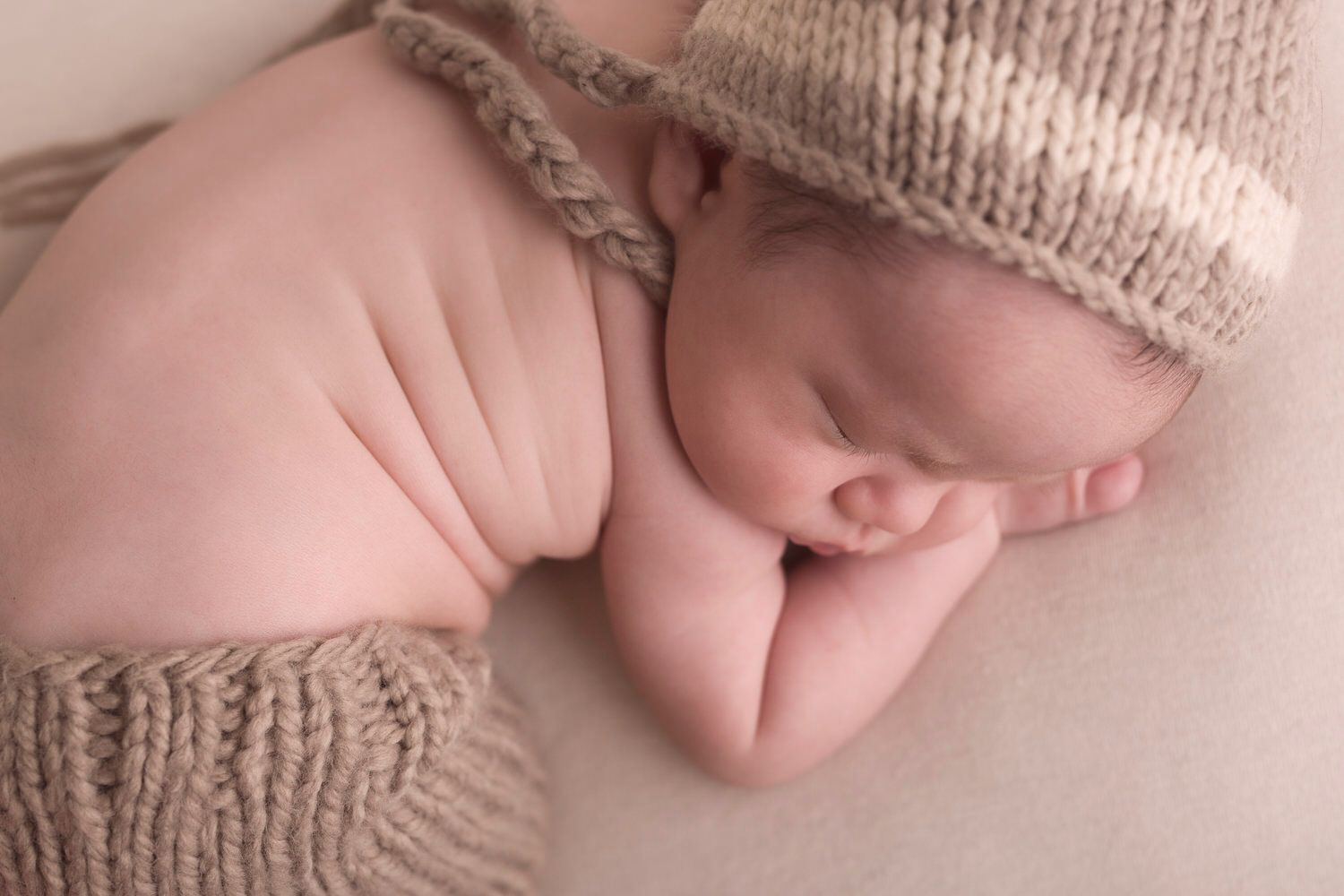 Newborn boy in knitted pants with matching hat. Sleeping with cheek on hand.