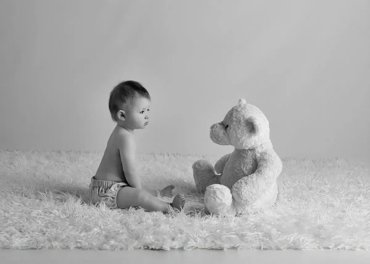 9 month old baby boy sitting in front of a teddy bear. Each looking at the other. Black and White.