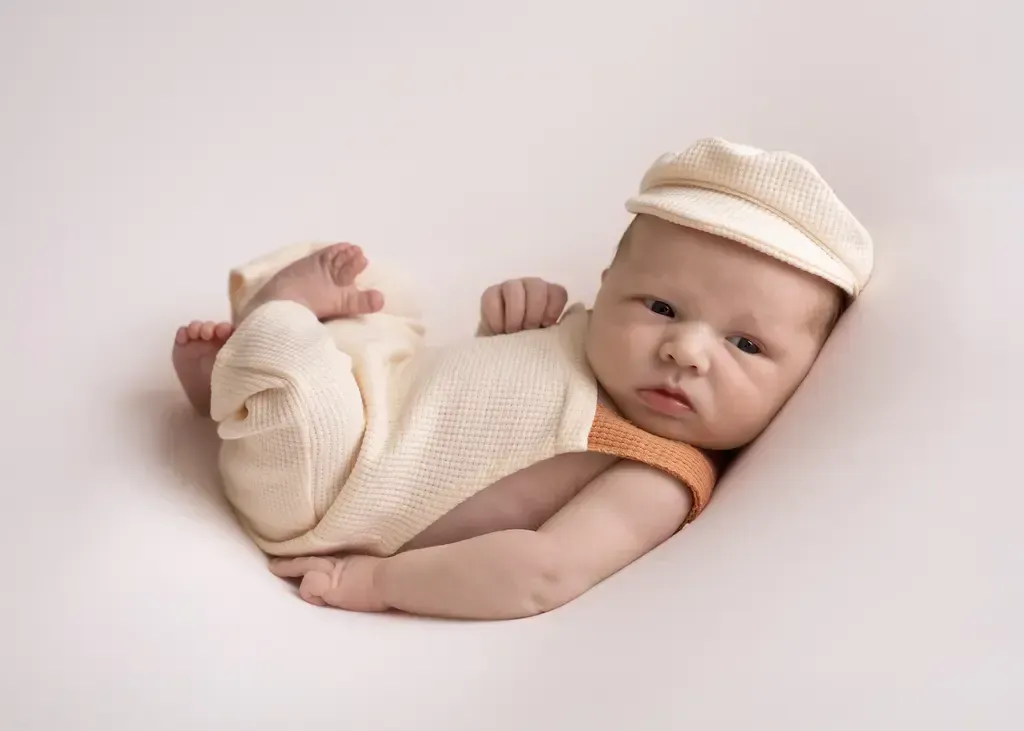 Newborn boy in cream overalls. Huck Finn pose