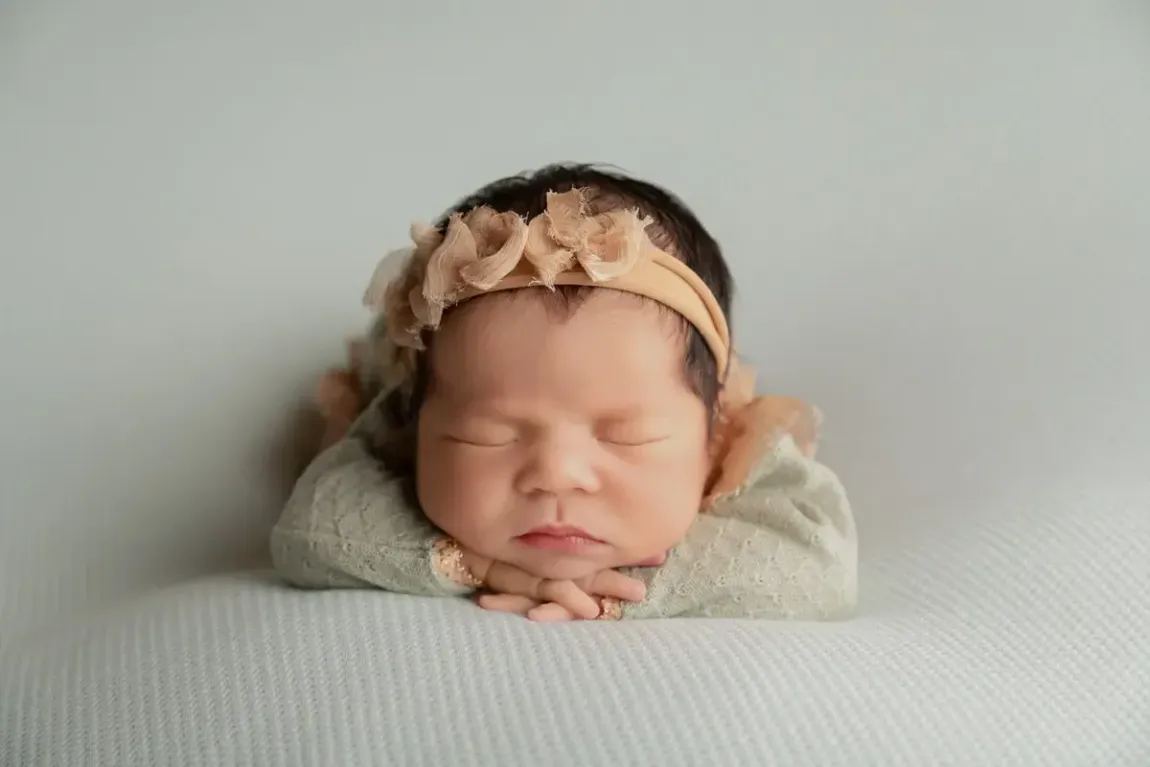 Newborn girl on sage background in matching outfit. Chin on hands.