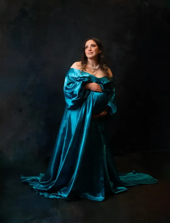 Maternity portrait in long flowing blue satin gown.