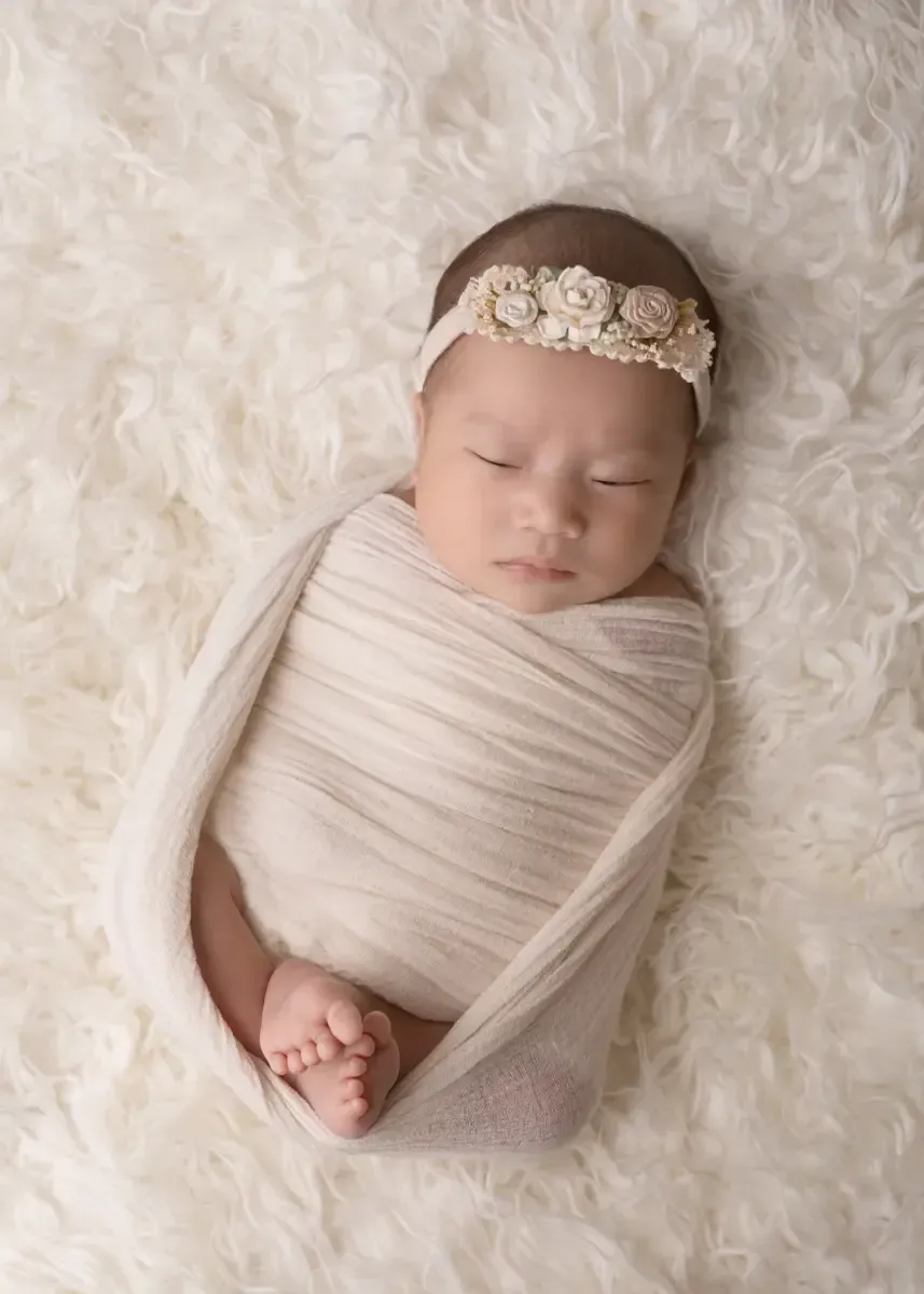 Newborn girl in cream wrap with feet showing.