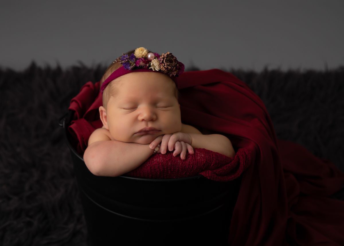 Newborn girl in bucket with wine colired headband