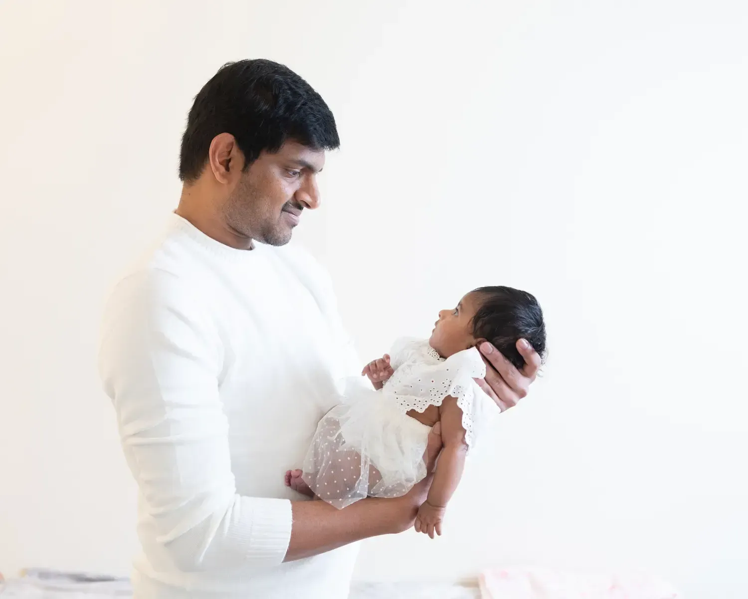 New dad holding newborn daughter. White background.