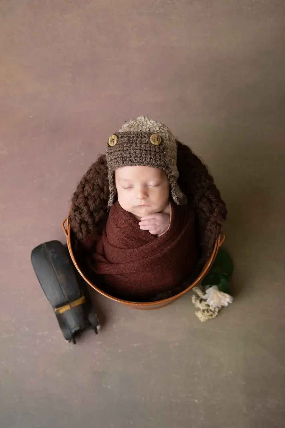 Newborn boy in aviator hat. Wrapped in bucket.