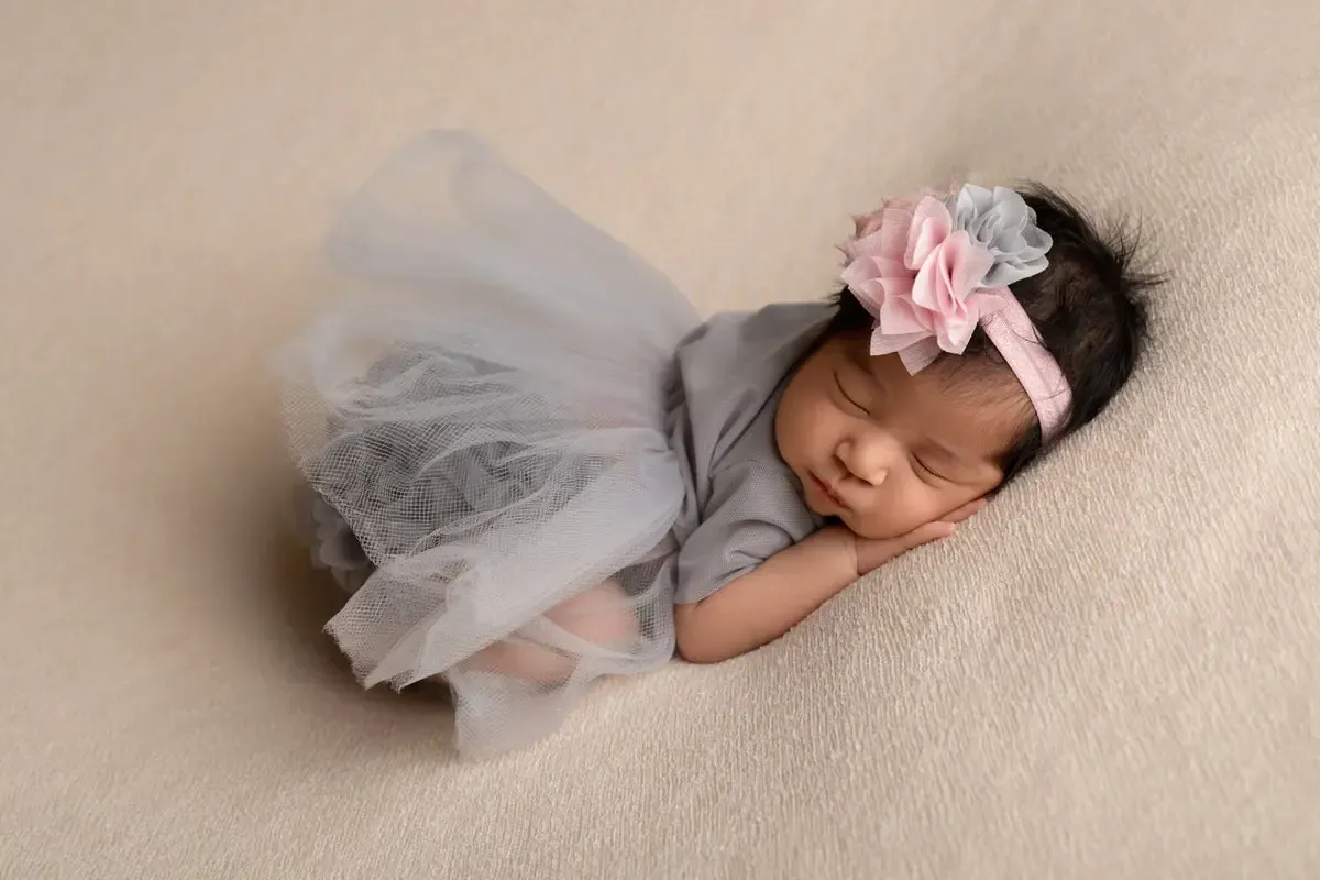 Newborn girl in grey tulle dress with matching headband. On her side with cheek on hand.