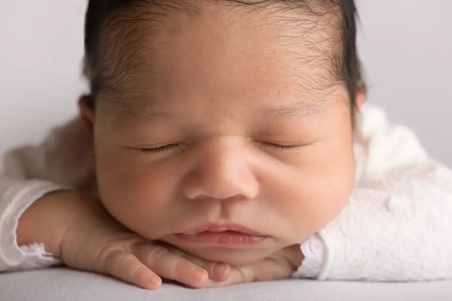 Newborn boy in white romper chin on hands. Close up.